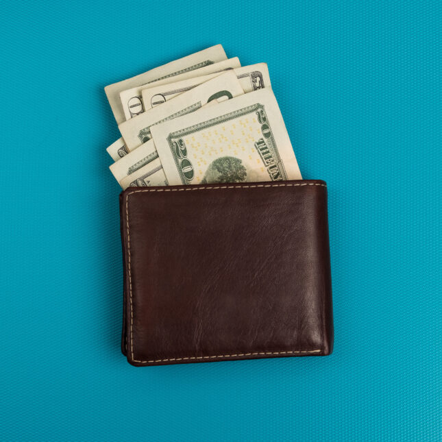 Photograph of a brown wallet with $20 bills coming out the top against a tel background. -- health policy coverage from STAT