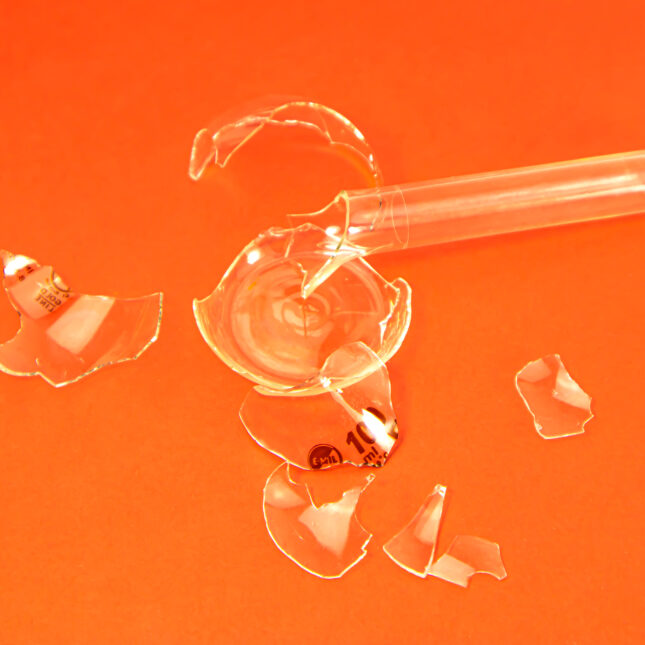 Broken laboratory glass on orange background. -- health policy coverage from STAT