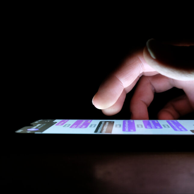 A finger hovers over a phone screen displaying chat messages in a dark room -- first opinion coverage from STAT