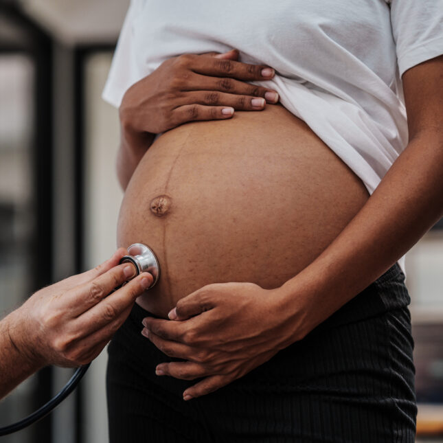 A doctor listens to a person's pregnant belly with a stethoscope — health coverage from STAT