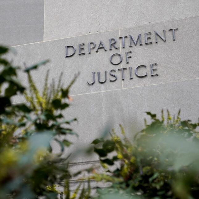 A building facade with the "DEPARTMENT OF JUSTICE" sign, framed behind trees -- insurance coverage from STAT