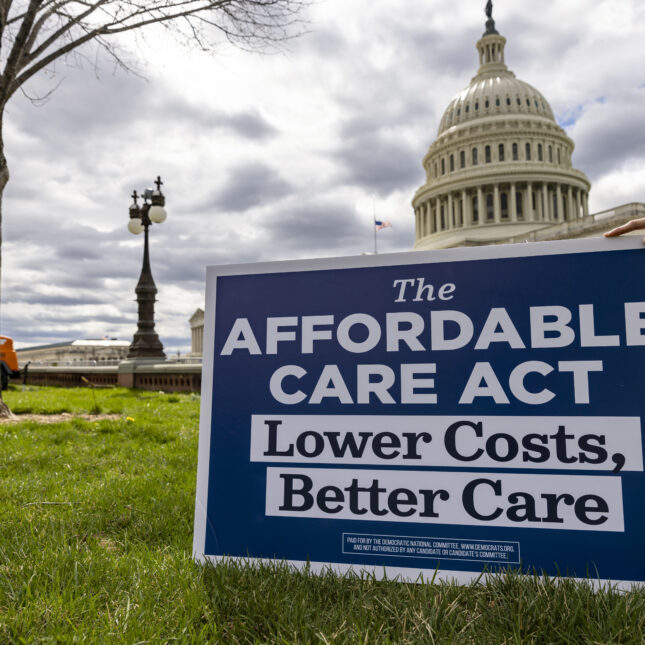 A person out of frame holds a sign up that reads "The affordable care act. Lower costs, better care" in front of the U.S. Capitol -- health policy coverage from STAT