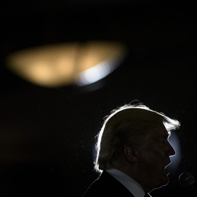 Silhouette of Donald Trump from the neck up speaking at a rally. --politics coverage from STAT