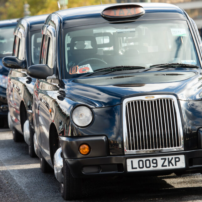 More than ten London taxi line up next to a line of traffic cones -- coverage from STAT